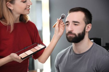 Çekici genç adamla kapalı çalışan profesyonel makyaj sanatçısı