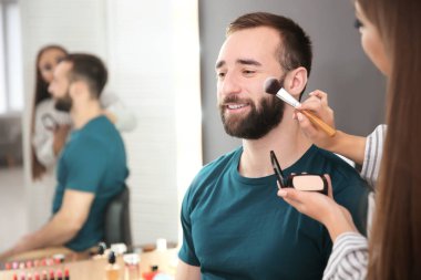 Çekici genç adamla kapalı çalışan profesyonel makyaj sanatçısı