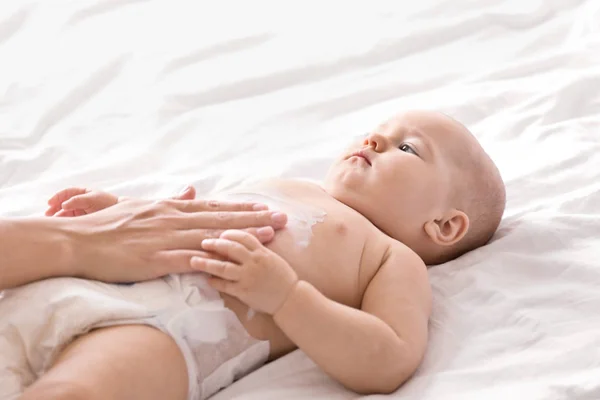 Mulher aplicando creme corporal em seu bebê dentro de casa — Fotografia de Stock