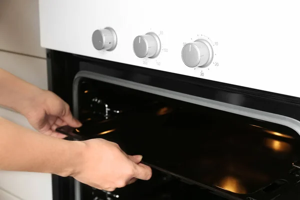 Jovem mulher tomando assadeira fora do forno elétrico moderno na cozinha — Fotografia de Stock