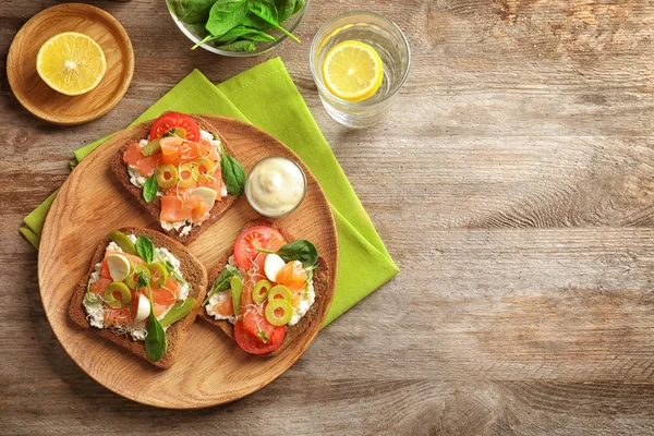 Des bruschettas savoureux aux olives et au saumon sur une assiette en bois — Photo