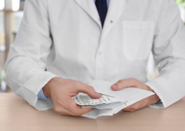 Мужчина-врач со взяткой на рабочем месте, крупный план
