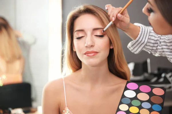 Artista de maquillaje profesional trabajando con atractiva mujer joven en el interior — Foto de Stock