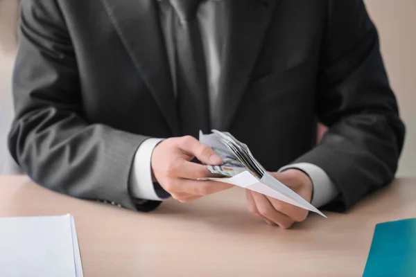 Geschäftsmann mit Geld im Umschlag am Tisch sitzend. Korruptionskonzept — Stockfoto