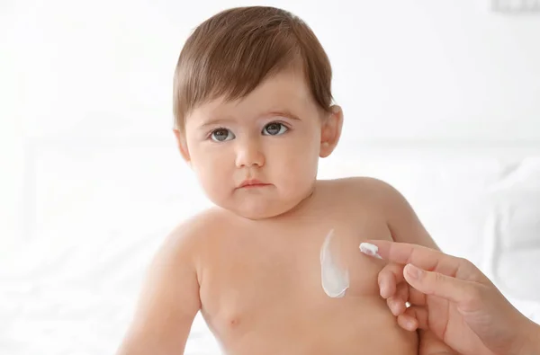 Woman applying body cream on her baby against light background — Stock Photo, Image