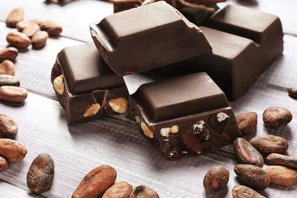 Pieces of chocolate and cocoa beans on wooden background, closeup — Stock Photo, Image