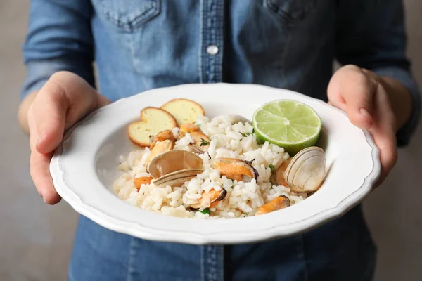 Jovem segurando prato com delicioso risoto de frutos do mar no fundo borrado — Fotografia de Stock