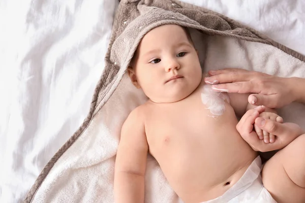 Женщина наносит крем для тела на своего ребенка в помещении — стоковое фото
