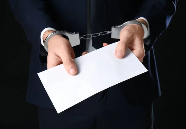 Empresário algemado segurando envelope com suborno em fundo preto — Fotografia de Stock