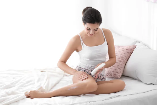 Νεαρή γυναίκα εφαρμογή κρέμα σώματος για το πόδι της στο υπνοδωμάτιο — Φωτογραφία Αρχείου