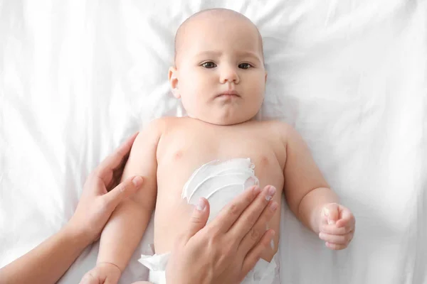 Mulher aplicando creme corporal em seu bebê dentro de casa — Fotografia de Stock