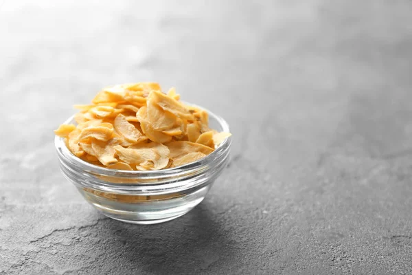 Glazen kom met gedroogde knoflook vlokken op grijze achtergrond — Stockfoto