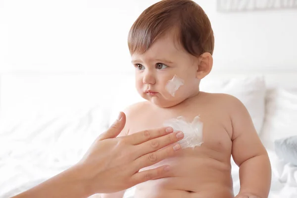 Mulher aplicando creme corporal em seu bebê contra fundo claro — Fotografia de Stock