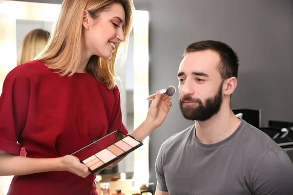Professionele make-up artist werken met aantrekkelijke jonge man binnenshuis — Stockfoto