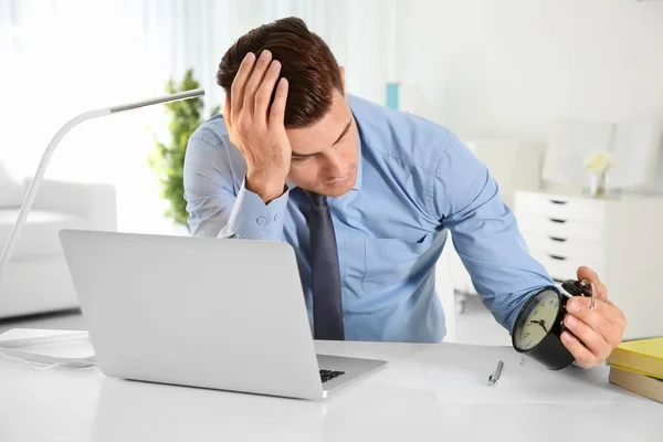 Troubled manager looking at alarm clock in office