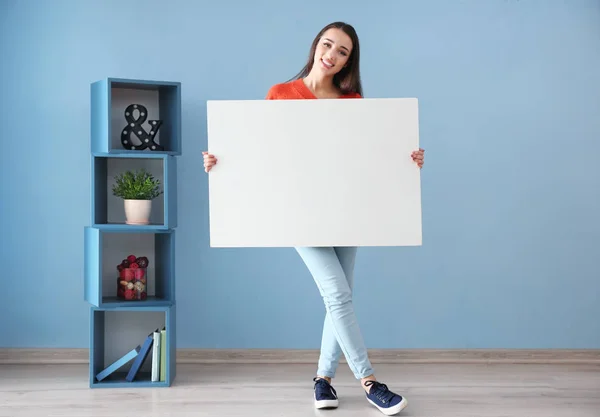 Красивая молодая женщина с чистой рекламной доской в помещении — стоковое фото