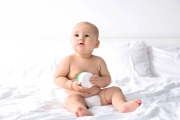 Niedliche Baby mit Glas Körpercreme auf dem Bett — Stockfoto