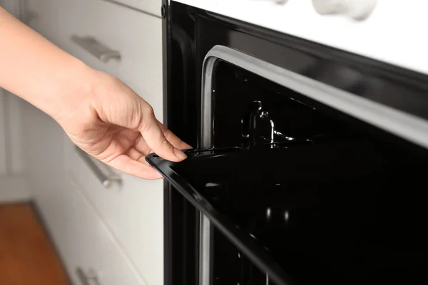 Young woman taking baking pan out of modern electrical oven in kitchen — Stock Photo, Image