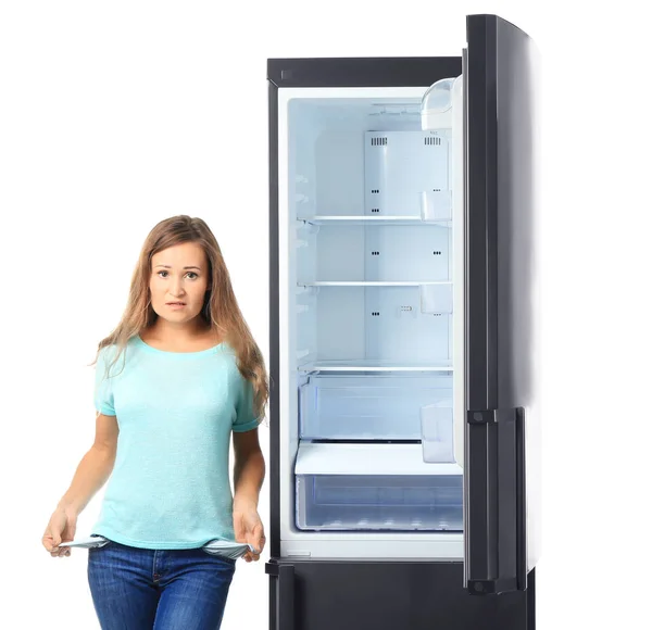 Donna che mostra tasche vuote vicino al frigorifero su sfondo bianco — Foto Stock