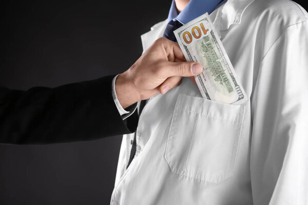 Бизнесмен кладет взятку в карман пальто врача на черном фоне
