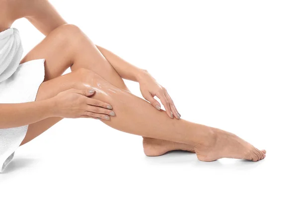 Kvinna applicera kroppskräm på hennes ben mot vit bakgrund, närbild — Stockfoto