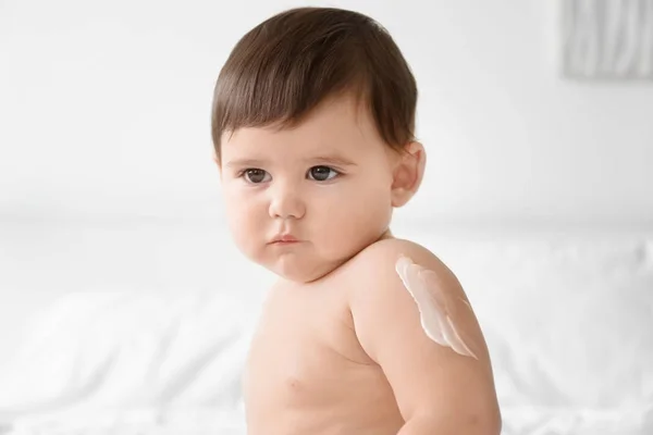 Bebê bonito com creme corporal no braço contra fundo leve — Fotografia de Stock
