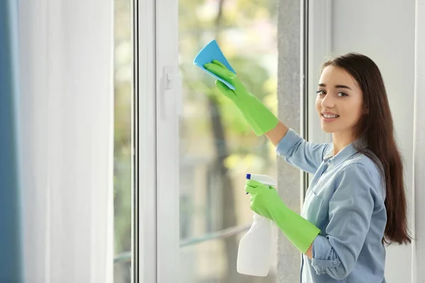 Young woman cleaning window glass in room