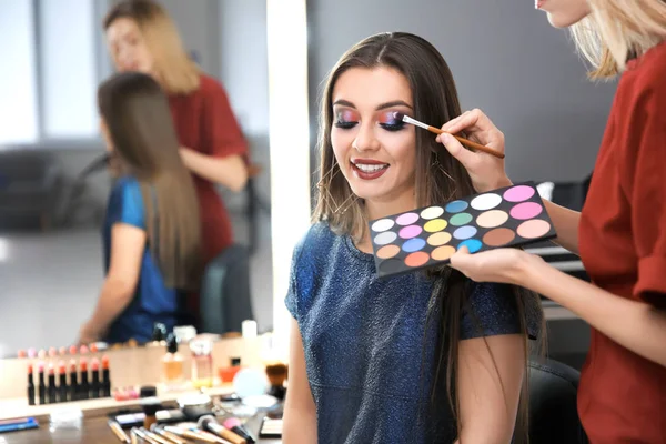 Professionell makeupartist arbetar med attraktiv ung kvinna inomhus — Stockfoto