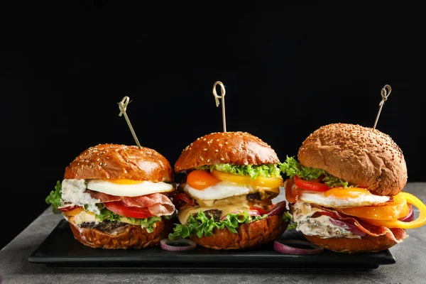 Plate with tasty burgers on table against black background — Stock Photo, Image