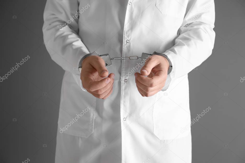 Male doctor in handcuffs on black background