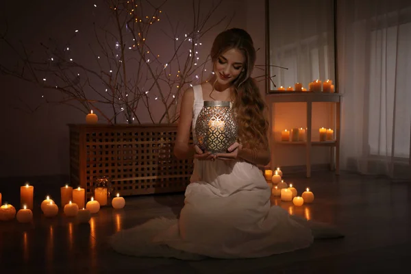 Beautiful young woman holding candle at home