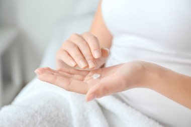 Young woman applying hand cream at home, closeup clipart