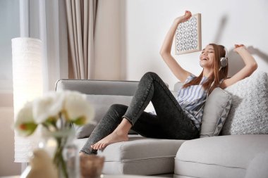 Evdeki kanepede dinlenirken müzik dinleyen genç bir kadın.