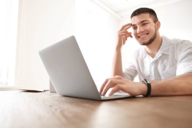 Genç adam evde dizüstü bilgisayar kullanıyor.