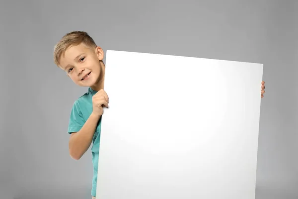 Lindo chico con tablero de publicidad en blanco sobre fondo gris —  Fotos de Stock