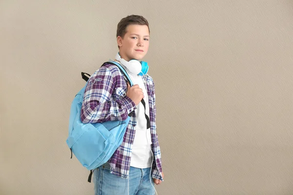 Dospívající chlapec s batohem a sluchátka na šedém pozadí — Stock fotografie