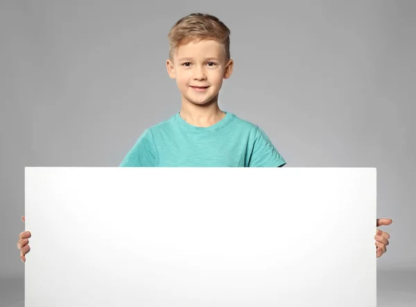 Rapaz bonito com placa de publicidade em branco no fundo cinza — Fotografia de Stock
