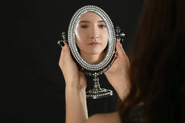 Young pretty girl looking in mirror on black background — Stock Photo, Image