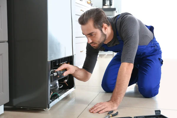 Male technician repairing refrigerator indoors