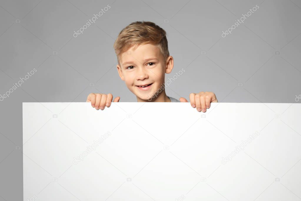 Cute boy with blank advertising board on grey background