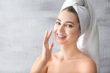 Young woman applying face cream on grey background clipart