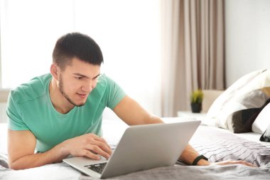 Genç adam evde dizüstü bilgisayar kullanıyor.