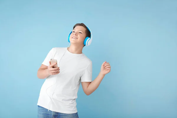 Adolescent garçon avec casque et smartphone écouter de la musique sur fond de couleur — Photo