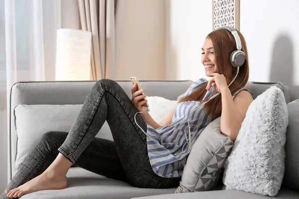 Mujer joven escuchando música mientras se relaja en el sofá en casa —  Fotos de Stock