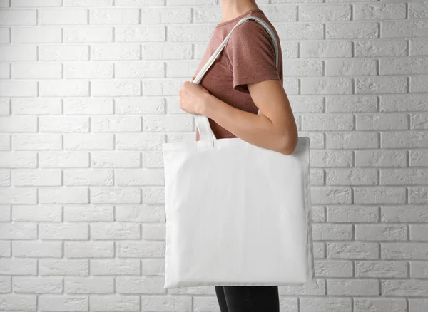 Woman with cotton bag near white brick wall. Mockup for design