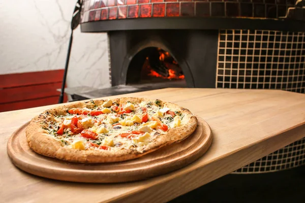 Tasty pizza on table against stove in kitchen