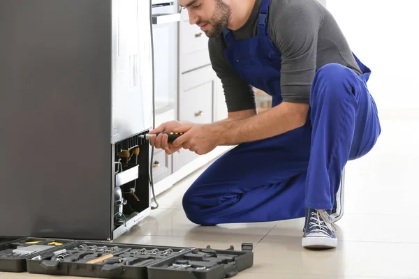 Male technician repairing refrigerator indoors