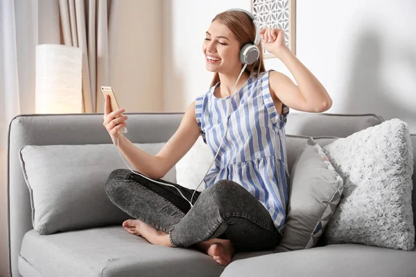 Giovane donna che ascolta musica mentre si rilassa sul divano di casa — Foto Stock