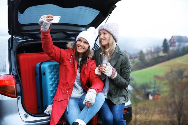 Turisti di sesso femminile che scattano selfie vicino all'auto in campagna — Foto Stock