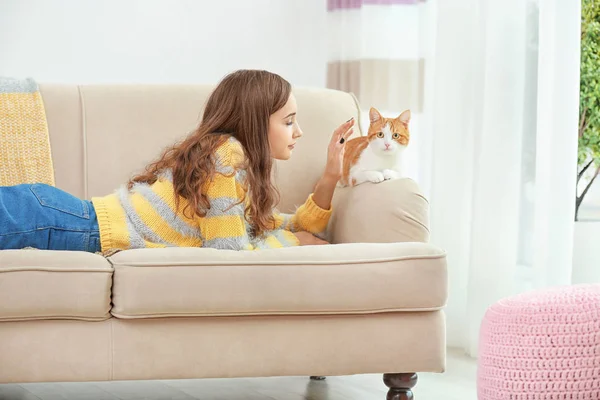 Красивая молодая женщина с милым котом на диване дома — стоковое фото